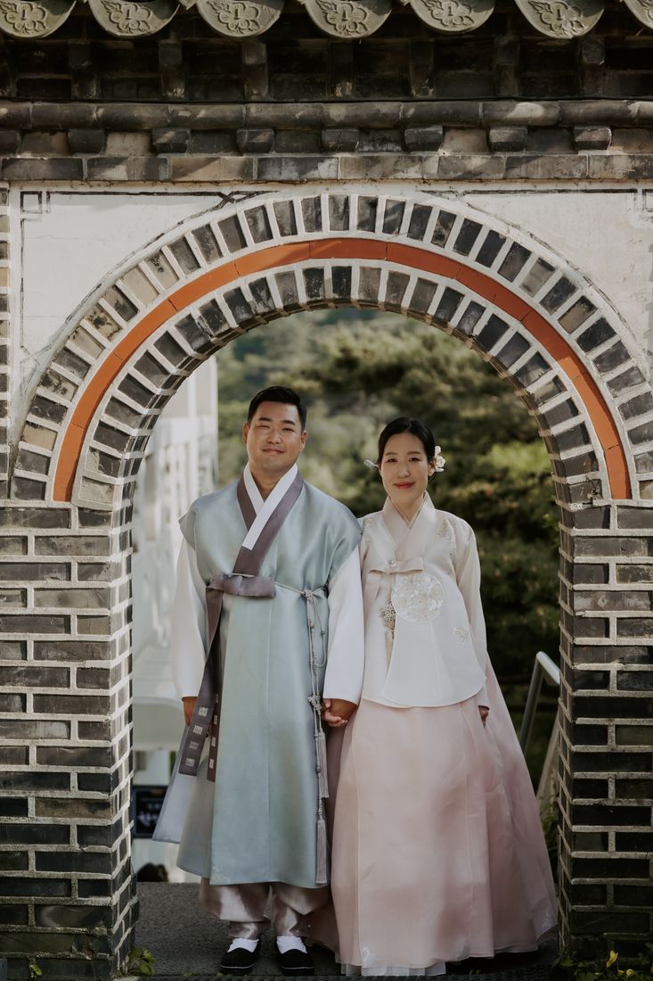 Tony and Eun Bi in hanbok under a stone archway on their wedding day